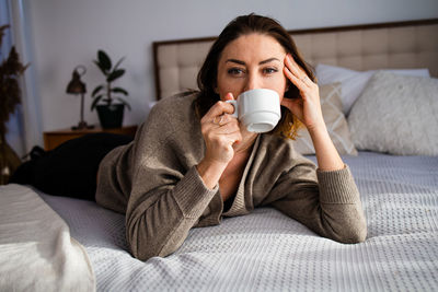 Young woman drinking coffee on bed at home