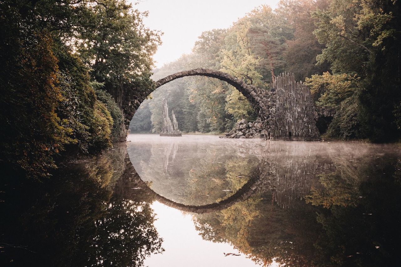 water, tree, reflection, river, tranquility, nature, lake, tranquil scene, waterfront, standing water, sky, scenics, canal, clear sky, beauty in nature, arch bridge, day, growth, outdoors, branch