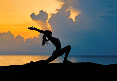 Silhouette of young woman doing yoga exercises on the rocks by the sea at sunrise