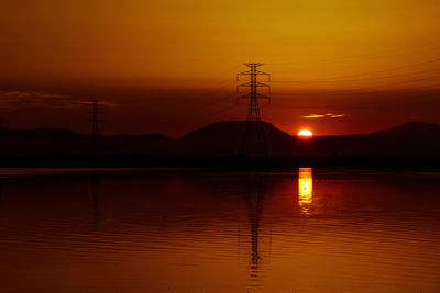 Calm sea with electricity pylon in distance at sunset