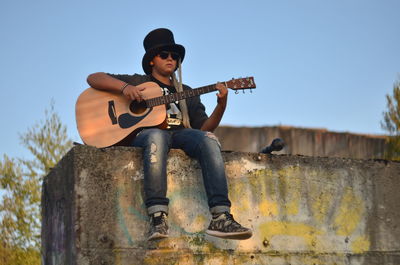 Full length of boy playing guitar while sitting on railing