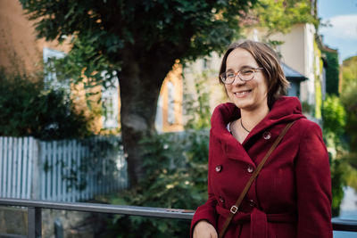 Smiling woman looking away while standing against trees