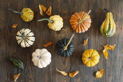 Multicolored pumpkins and dry autumn leaves on wooden background.