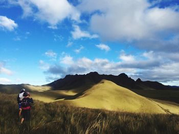 Rear view of friends walking on landscape against cloudy sky