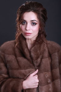 Portrait of beautiful young woman wearing fur coat against black background