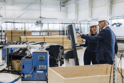 Manager explaining machine to colleague standing in factory