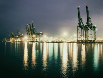 Illuminated harbor by sea against sky at night