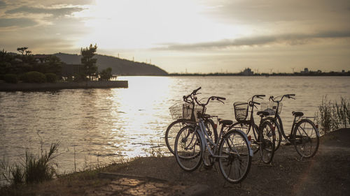 Bicycle by river against sky during sunset