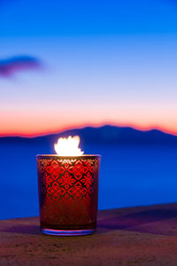 Close-up of illuminated tea light against sky during sunset