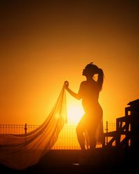 Silhouette woman standing against orange sky