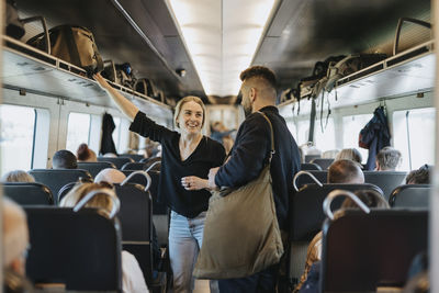 Smiling woman talking to man while standing between seats in train