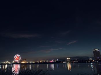 Illuminated city by river against sky at night