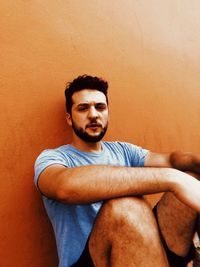 Portrait of young man sitting against wall