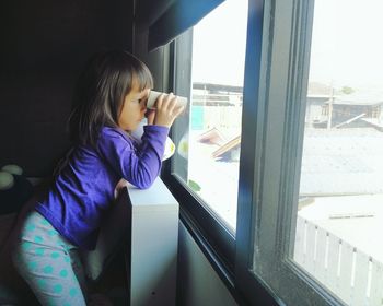 Side view of girl looking through window