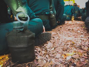 Close-up of water bottle by low section of army soldiers sitting outdoors