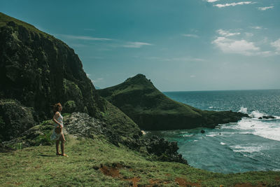 Young woman standing on rock by sea against sky