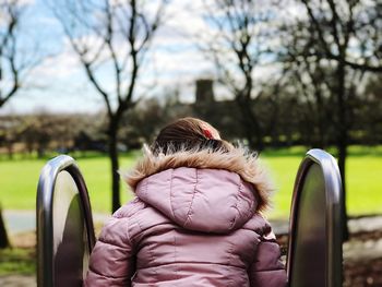 Rear view of girl wearing warm clothing amidst railing against sky