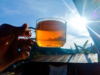 Midsection of person holding drink against sky