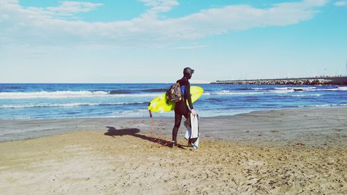 Person with surfboard walking at beach against sky