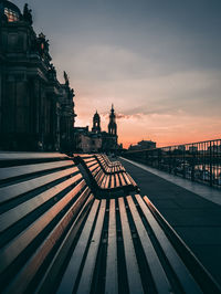 Empty benches in city against sky during sunset