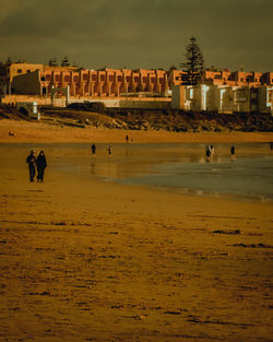 People at beach against sky during sunset