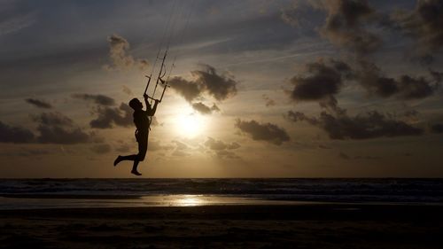 Silhouette man kiteboarding at beach during sunset