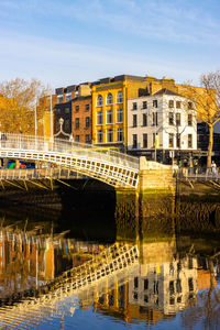 Bridge over river by buildings against sky