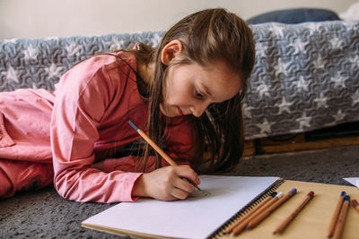 The girl after school plays at home, draws with pencils and felt-tip pens