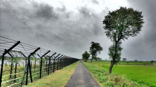 Road passing through field against cloudy sky