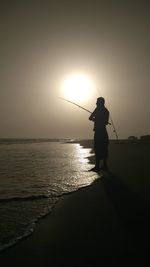 Silhouette man standing in sea against sky during sunset