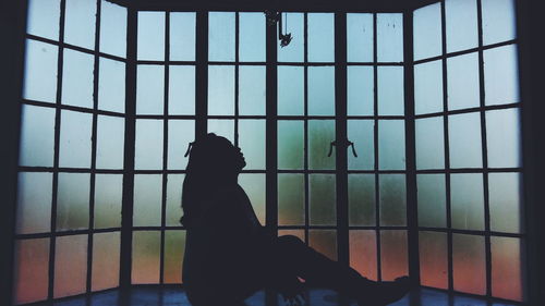 Silhouette woman sitting by glass window