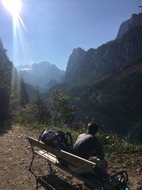 People sitting on bench looking at mountains against sky