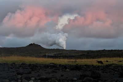 Smoke emitting from geothermal pool on landscape against sky