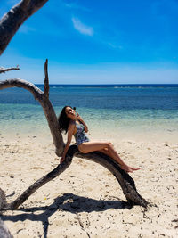 Portrait of woman siting on driftwood at beach against sky