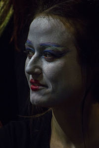 Close-up portrait of young woman with make up against black background