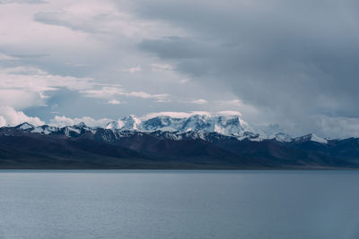 Scenic view of river by snowcapped mountains against cloudy sky