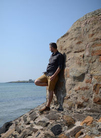 Man standing on rock by sea against clear sky