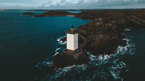 Lighthouse amidst sea and buildings against sky