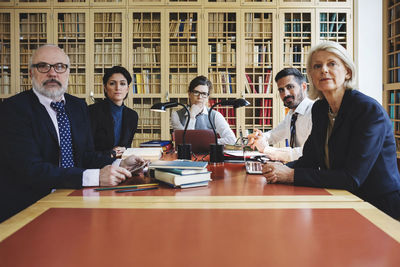 Portrait of lawyers sitting in board room against bookshelf