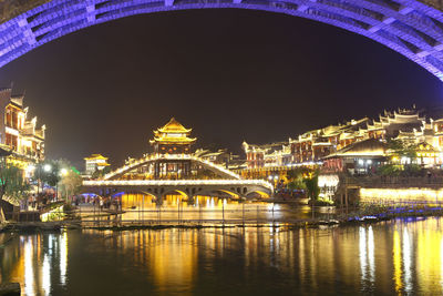 Illuminated bridge over river against sky at night