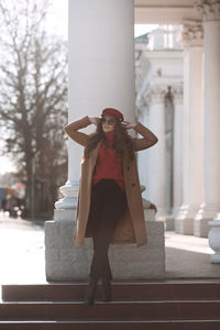 Stylish woman wearing winter coat and hat pose on street over city background. girl resting outdoor