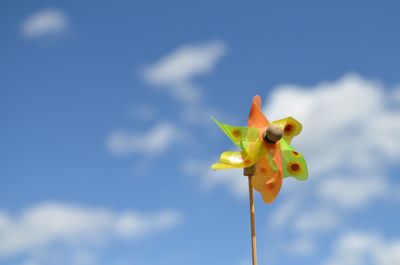 Low angle view of pinwheel toy against cloudy sky on sunny day