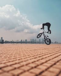 Man riding bicycle in city against sky