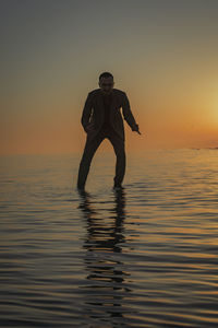 Man standing in sea against sky during sunset
