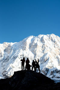 People on snowcapped mountain against clear blue sky