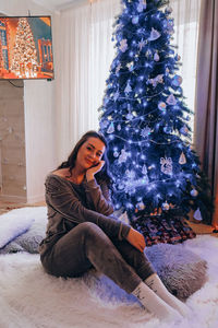 Beautiful young girl sitting next to the christmas tree. new year decoration. home interior. winter
