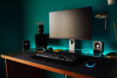 Modern stylish black gaming computer with keyboard and speakers placed on table near joystick lamp and stationery