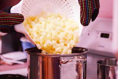 Cropped image of hands putting boiled potatoes in container at kitchen