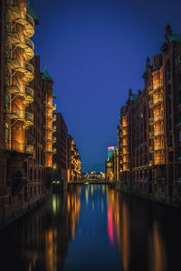 Illuminated buildings by river against sky at night