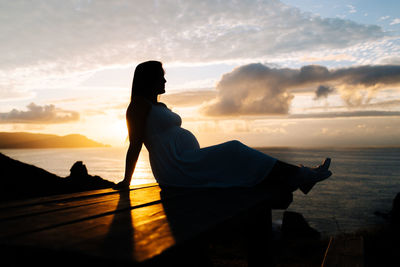 Silhouette woman on shore against sky during sunset